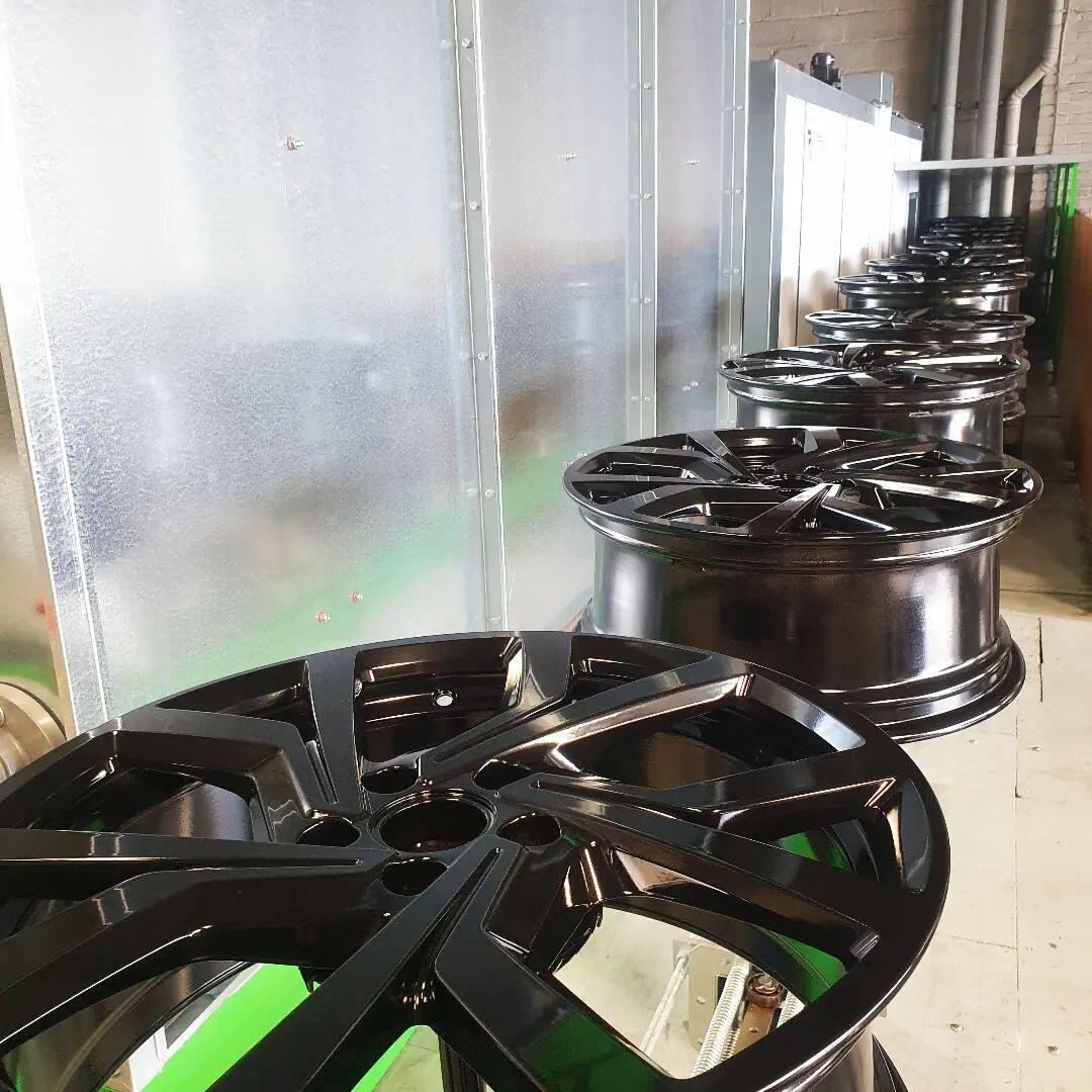Stack of freshly powder coated gloss black alloy wheels ready for collection